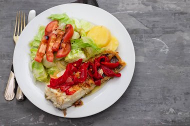 Kırmızı biberli morina balığı, beyaz tabakta patates ve salata.