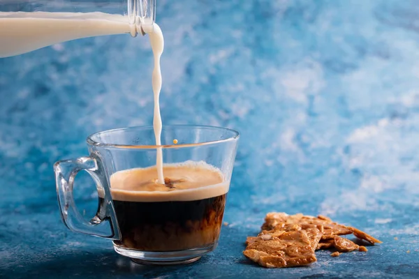Mléko nalévání na kávu na modrém pozadí — Stock fotografie