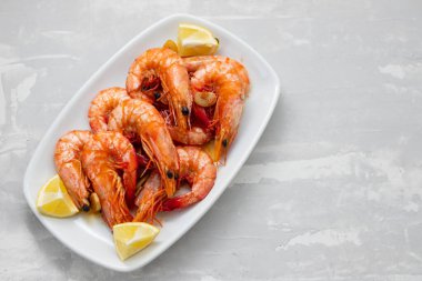 Beyaz tabakta seramik zemin üzerinde limonlu haşlanmış karides