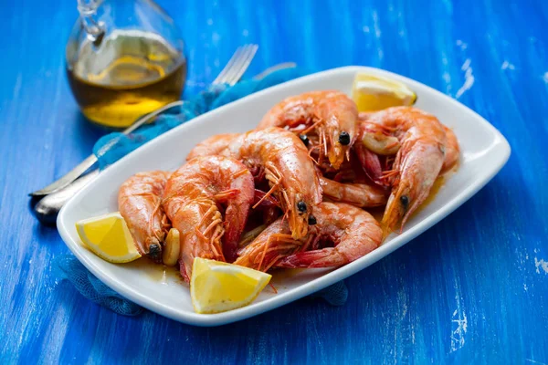 Camarones cocidos con limón sobre plato blanco sobre fondo de madera azul —  Fotos de Stock