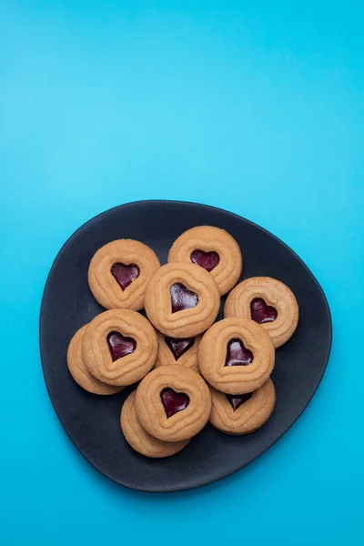 Biscotti con cuori su piatto scuro su sfondo blu — Foto Stock