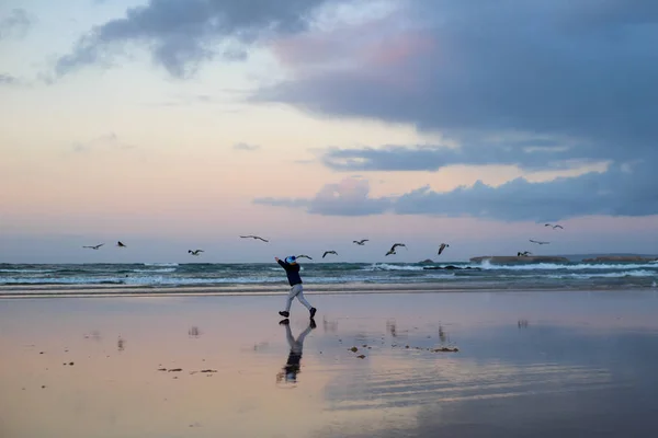 Αγόρι τρέχει με τα πουλιά στη χειμερινή παραλία κοντά στον ωκεανό — Φωτογραφία Αρχείου