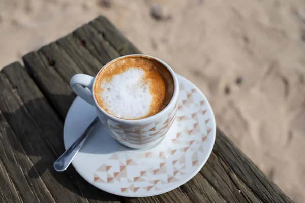 Kaffee mit Milch auf Holztisch am Strand mit Sand — Stockfoto