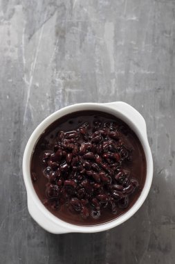 Seramik zemin üzerinde beyaz kasede kaynamış siyah fasulye.