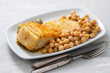 Bezelyeli kızarmış morina balığı ve seramik arka planda beyaz tabakta zeytin.