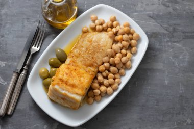 Bezelyeli kızarmış morina balığı ve seramik arka planda beyaz tabakta zeytin.