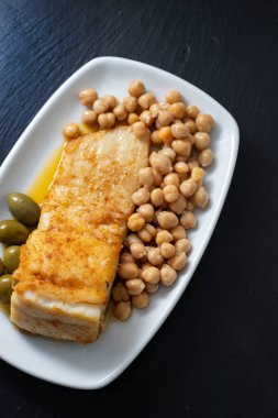 Bezelyeli kızarmış morina balığı ve seramik arka planda beyaz tabakta zeytin.