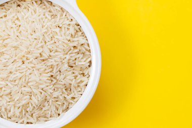 uncooked white rice in white bowl on yellow background clipart