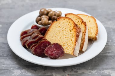 Tütsülenmiş sosisli mısır ekmeği ve beyaz tabakta zeytin.