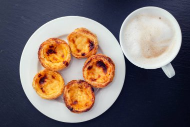 Beyaz tabakta Portekiz yumurtalı tart pastel de nata ve sütlü kahve.