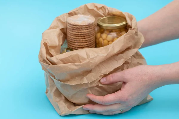 canned food, cookies, chickpea in paper bag with hands on blue background