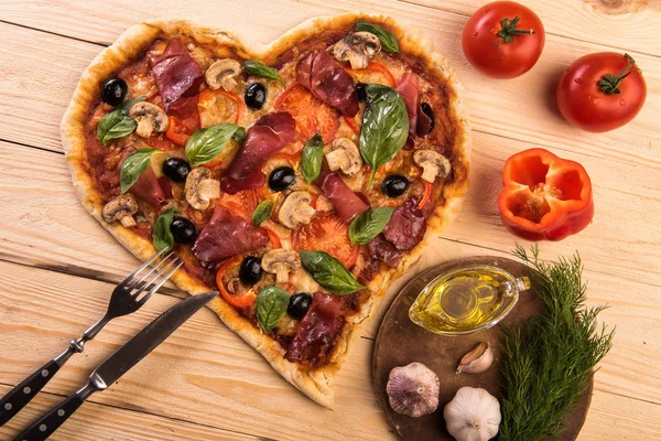 Pizza heart love Valentines Day romantic Italian restaurant dinner food. Prosciutto, olives, tomatoes, parsley, basil and mozzarella cheese meal on wooden table