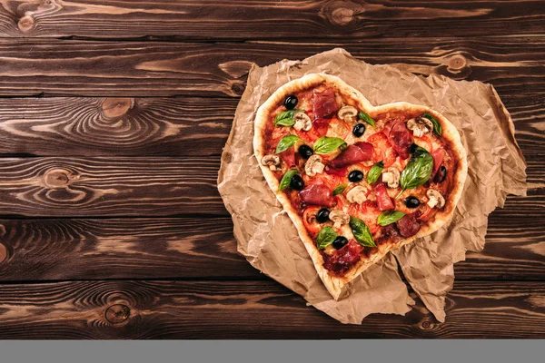Heart shaped pizza with tomatoes and prosciutto for Valentines Day on vintage wooden background. Food concept of romantic love