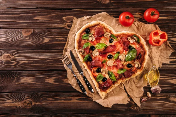 Heart shaped pizza with tomatoes and prosciutto for Valentines Day on vintage wooden background. Food concept of romantic love