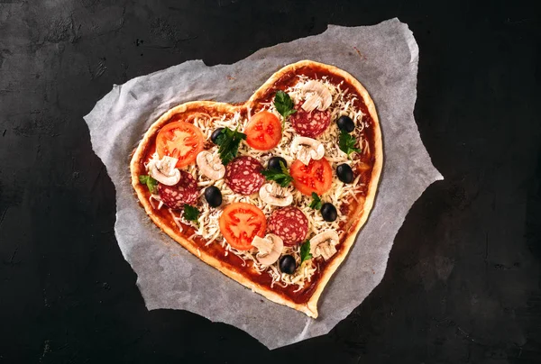 Heart shaped pizza with tomatoes and mozzarella for Valentines Day on vintage black background. Food concept of romantic love