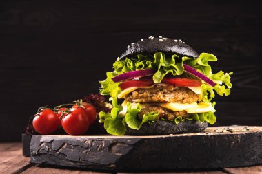 Lezzetli ev yapımı vegan siyah burger iki nohut Beşamel sos, domates, peynir, soğan ve ahşap masa, koyu arka plan üzerinde salata ile.