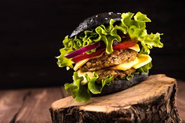 Lezzetli ev yapımı vegan siyah burger iki nohut Beşamel sos, domates, peynir, soğan ve ahşap masa, koyu arka plan üzerinde salata ile.