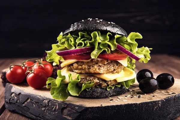 Leckere hausgemachte vegane schwarze Burger mit zwei Kichererbsenschnitzeln, Tomaten, Käse, Zwiebeln und Salat auf Holztisch, dunkler Hintergrund. — Stockfoto