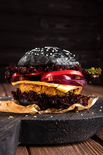 Homemade vegetarian black chickpea burger with one cutlet, tomato, cheese, dark lettuce and purple onion on rustic wooden table