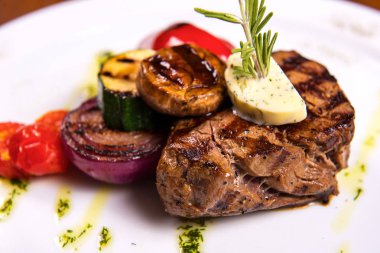 Biberiye ve kızarmış sebze peynir beyaz plaka üzerinde kalın biftek. yakın çekim