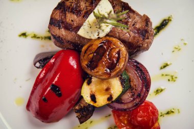 Biberiye ve kızarmış sebze peynir beyaz plaka üzerinde kalın biftek. görünümünün üst