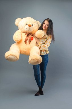 Büyük ayıcık yumuşak oyuncak gülümseyen ve gri arka plan üzerinde oynarken mutlu ile genç güzel kız