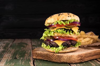 Siyah ahşap rustick arka plan üzerinde biftek ve kızarmış patates sebze ile büyük sulu hamburger. Tonda vintage