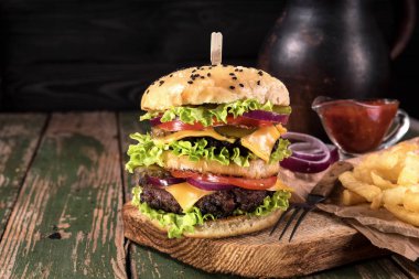 Siyah ahşap rustick arka plan üzerinde biftek ve kızarmış patates sebze ile büyük sulu hamburger. Tonda vintage