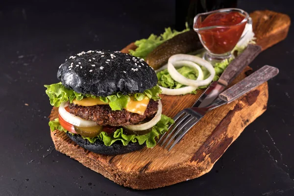 Frische hausgemachte Burger auf hölzernem Servierbrett mit Gabel und Messer Tomatensauce auf dunklem Hintergrund — Stockfoto