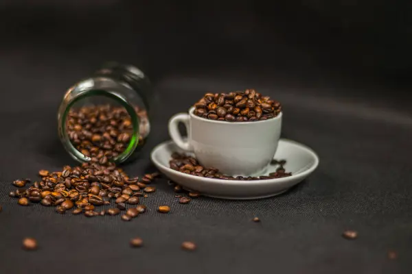 Granos de café aromáticos en una taza blanca y granos de café derramados fr — Foto de Stock
