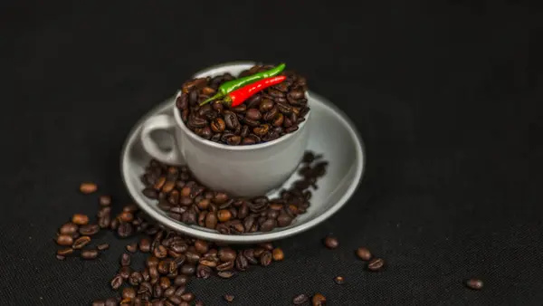 Αρωματικοί κόκκοι καφέ σε λευκό φλιτζάνι με διακόσμηση από οξεία κόκκινο — Φωτογραφία Αρχείου