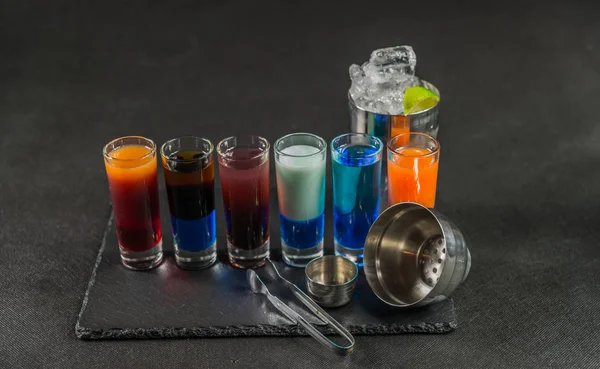 Šest různých barevných zastřelených nápojů, seřazeni na černý kámen pla — Stock fotografie