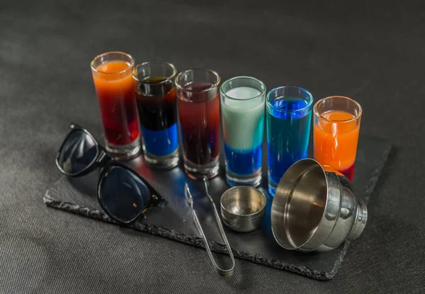 Šest různých barevných zastřelených nápojů, seřazeni na černý kámen pla — Stock fotografie