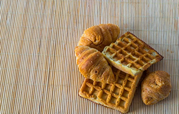 Croissants frescos y deliciosos gofres en estera de bambú, panadería —  Fotos de Stock