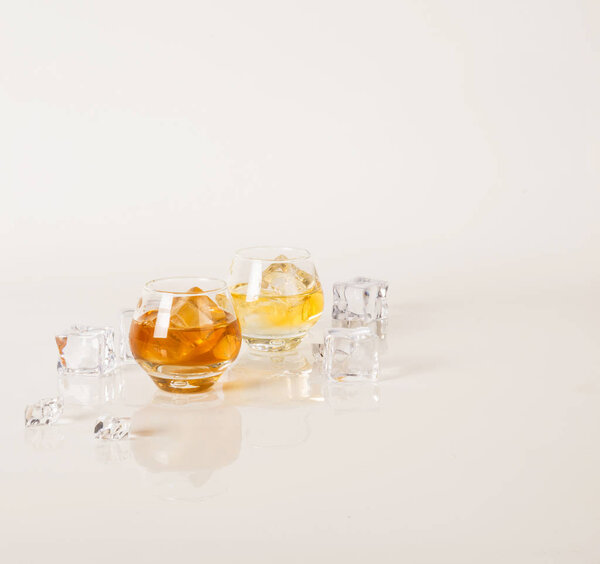 Two low round glasses with different golden alcohols and ice cub