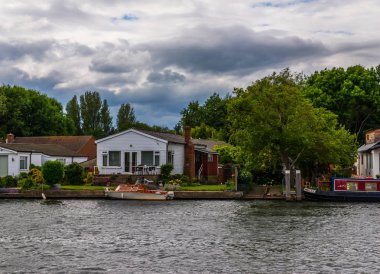 Geniş nehir ve evleri sahilinde demirli deniz araçları, yeşil vegetati