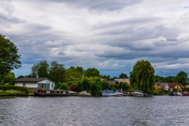 Geniş nehir ve evleri sahilinde demirli deniz araçları, yeşil vegetati