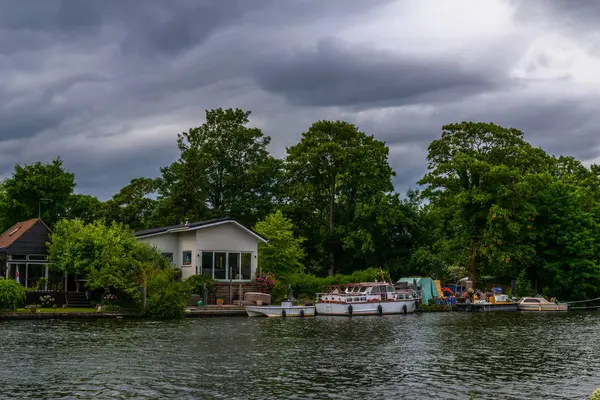 Широкая река и дома на берегу, пришвартованные лодки, зеленые деревья. — стоковое фото