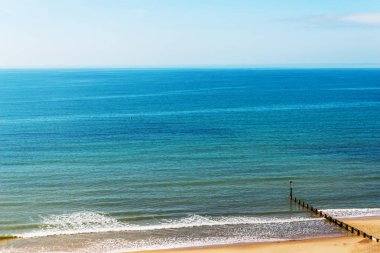Bir kumsal, mavi okyanus ve sarı kum, güneşli kazıklara dock