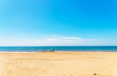 Bir kumsal, mavi okyanus ve sarı kum, güneşli kazıklara dock