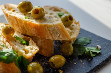 Zeytinle doldurulmuş baget, taze yeşil zeytin ve maydanozla kesilmiş, taş tabakta servis edilmiş, sağlıklı aperatif.