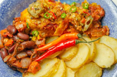 Kırmızı biberli tavuk göğsü fileto ve peynirli domates sosu yanında kızarmış patates dilimleri ve mavi tabakta naneli fasulye salatası, Meksika yemeği.