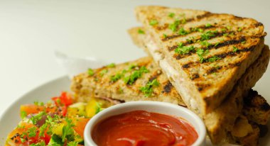 Tavuk göğsü ve kayın ağacı tütsülenmiş pastırmalı el yapımı sandviç. Karışık salata, domates sosu ve sağlıklı bir yemekle servis ediliyor.