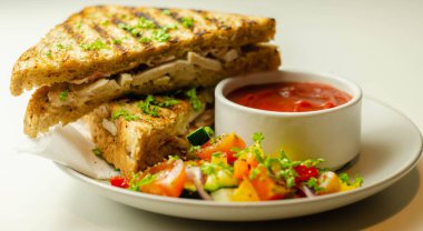 Tavuk göğsü ve kayın ağacı tütsülenmiş pastırmalı el yapımı sandviç. Karışık salata, domates sosu ve sağlıklı bir yemekle servis ediliyor.