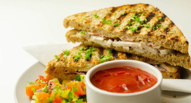 Tavuk göğsü ve kayın ağacı tütsülenmiş pastırmalı el yapımı sandviç. Karışık salata, domates sosu ve sağlıklı bir yemekle servis ediliyor.