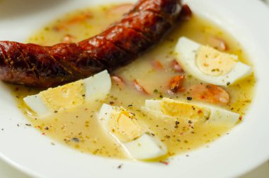 Geleneksel Polonya ekşi çorbası, sosis ve yumurtalar seramik kasede, Doğu Avrupa yemeği.