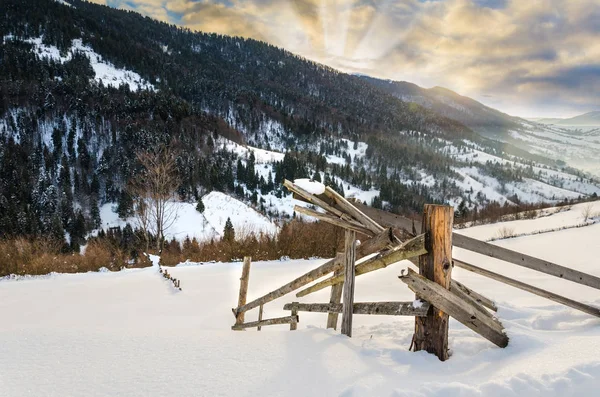 Wooden fences foreground. Winter mountain view at dawn, the sun'