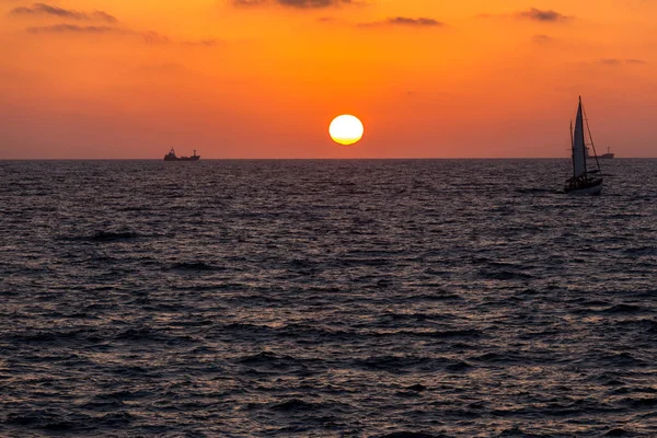 Желто-красный закат на море с видом на парусник — стоковое фото