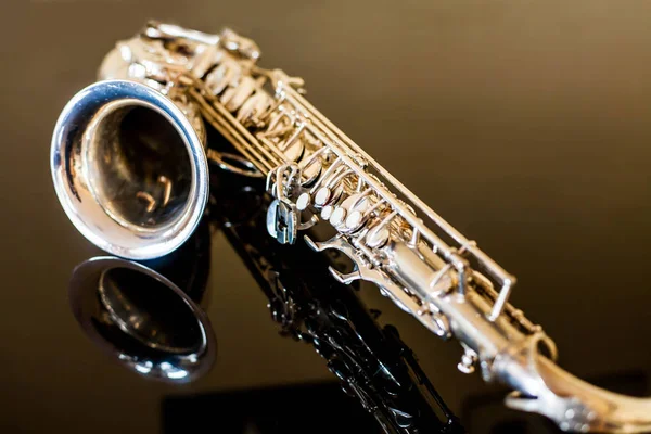 Saxophone tenor. Woodwind Classical Instrument. Jazz, blues, classics. Music. Saxophone on a black background. Black mirror surface. Music styles — Stock Photo, Image