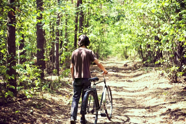 Een man met een fiets in het bos. Zomer bos, groene bladeren, groene bomen en gras. Old school fiets Stockfoto
